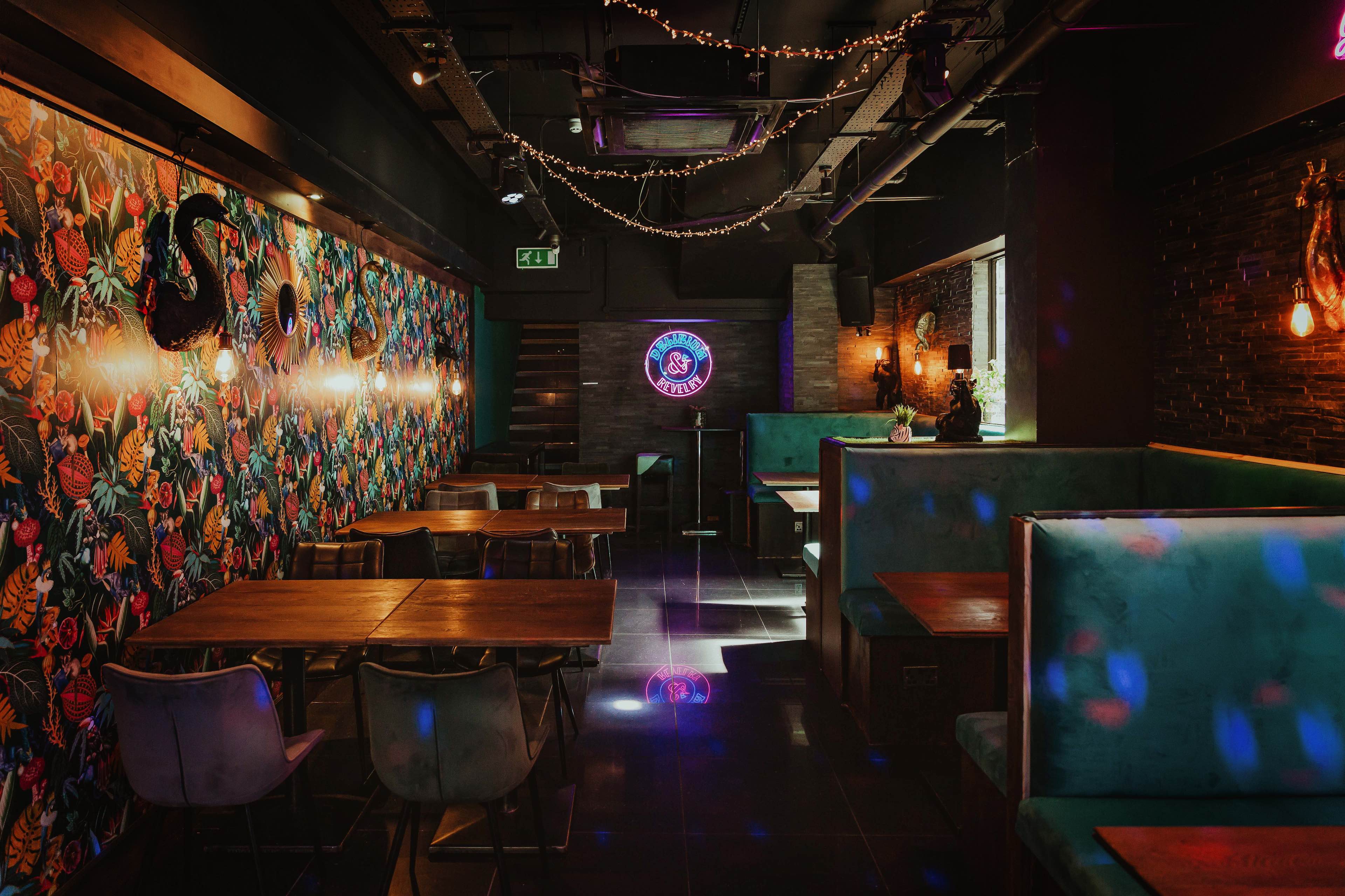 Several comfy booths and tables glowing under a neon sign.